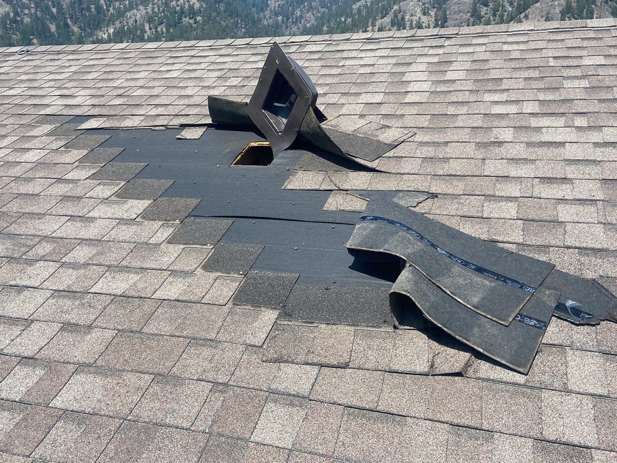 Asphalt shingles peeled back and a roof vent torn out by wind