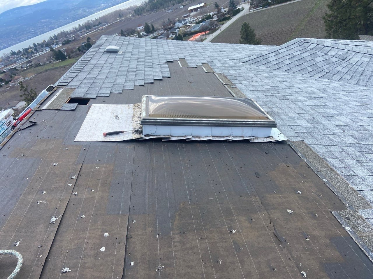 A roof opened up around a skylight during a storm-damage repair, Okanagan Lake beyond